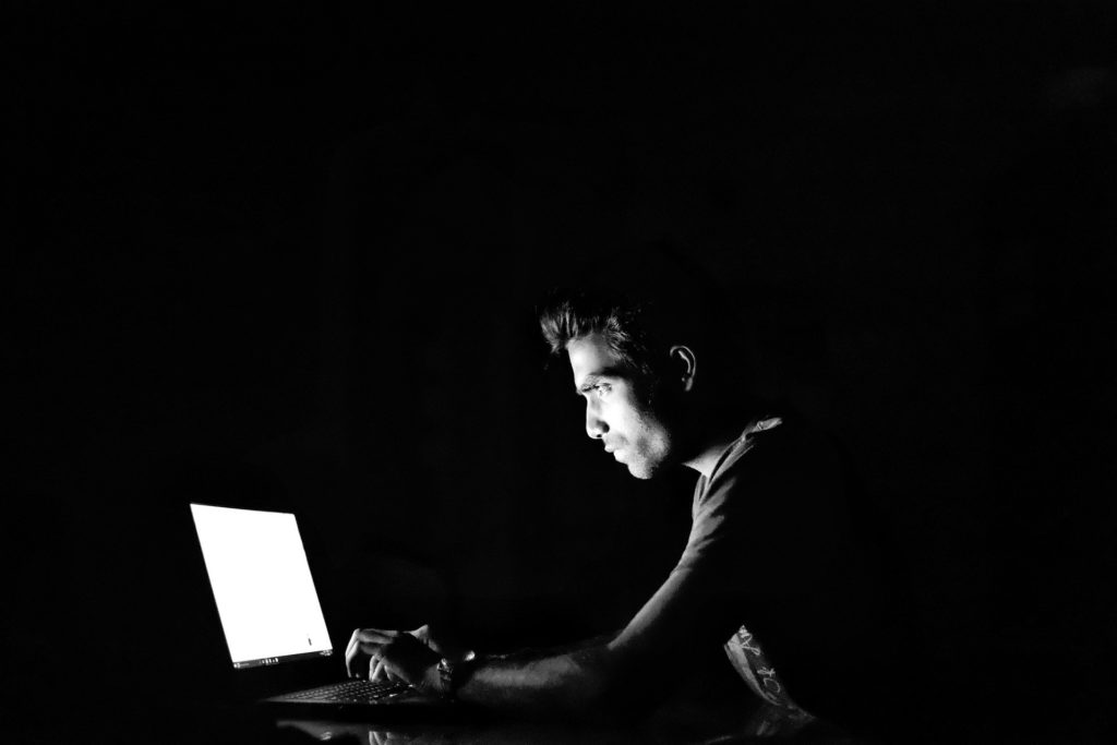 Sprawdzanie sklepu przez internet (opis zdjęcia: mężczyzna trzyma palce na klawiaturze przed ekranem laptopa, który rozjaśnia mrok i twarz), fot. iAmMrRob Robinraj Premchand Pixabay 2903156 https://pixabay.com/pl/photos/h-2903156/
