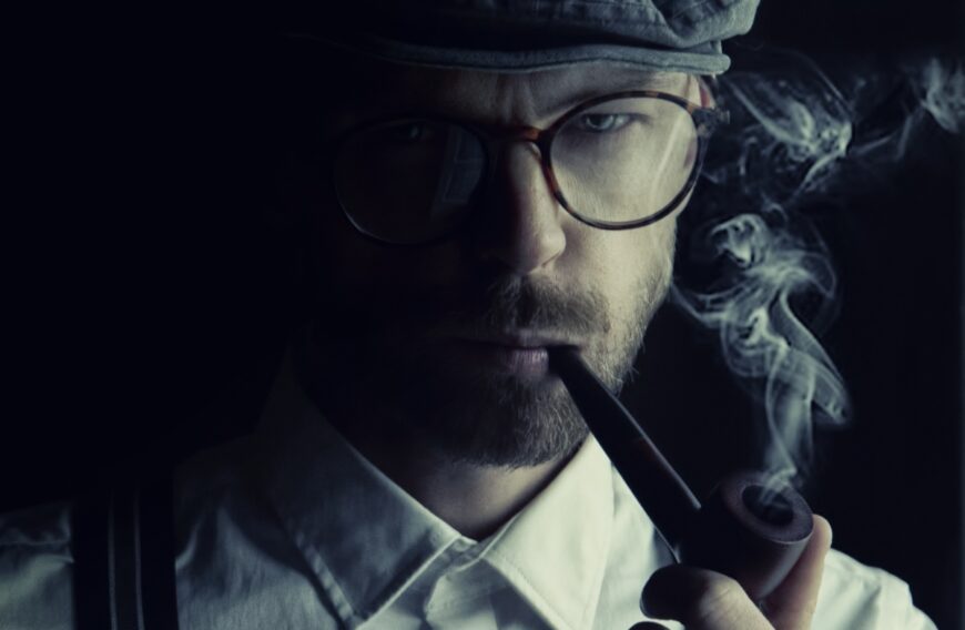tropienie przodków – genealog detektyw? [opis zdjęcia dla niewidzących: młody mężczyzna stylizowany na Sherlocka Holmesa w koszuli, na szelkach, w okularach, z beretem, palący fajkę] fot. „Sammy-Sander” Sam Williams Pixabay 4125016